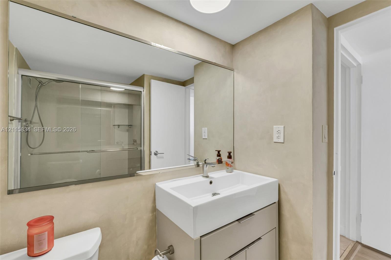 Wall-to-wall vanity mirror, square vessel sink with single-lever chrome faucet, modern floating vanity cabinet with metal hardware, and glass-enclosed shower with adjustable handheld fixture