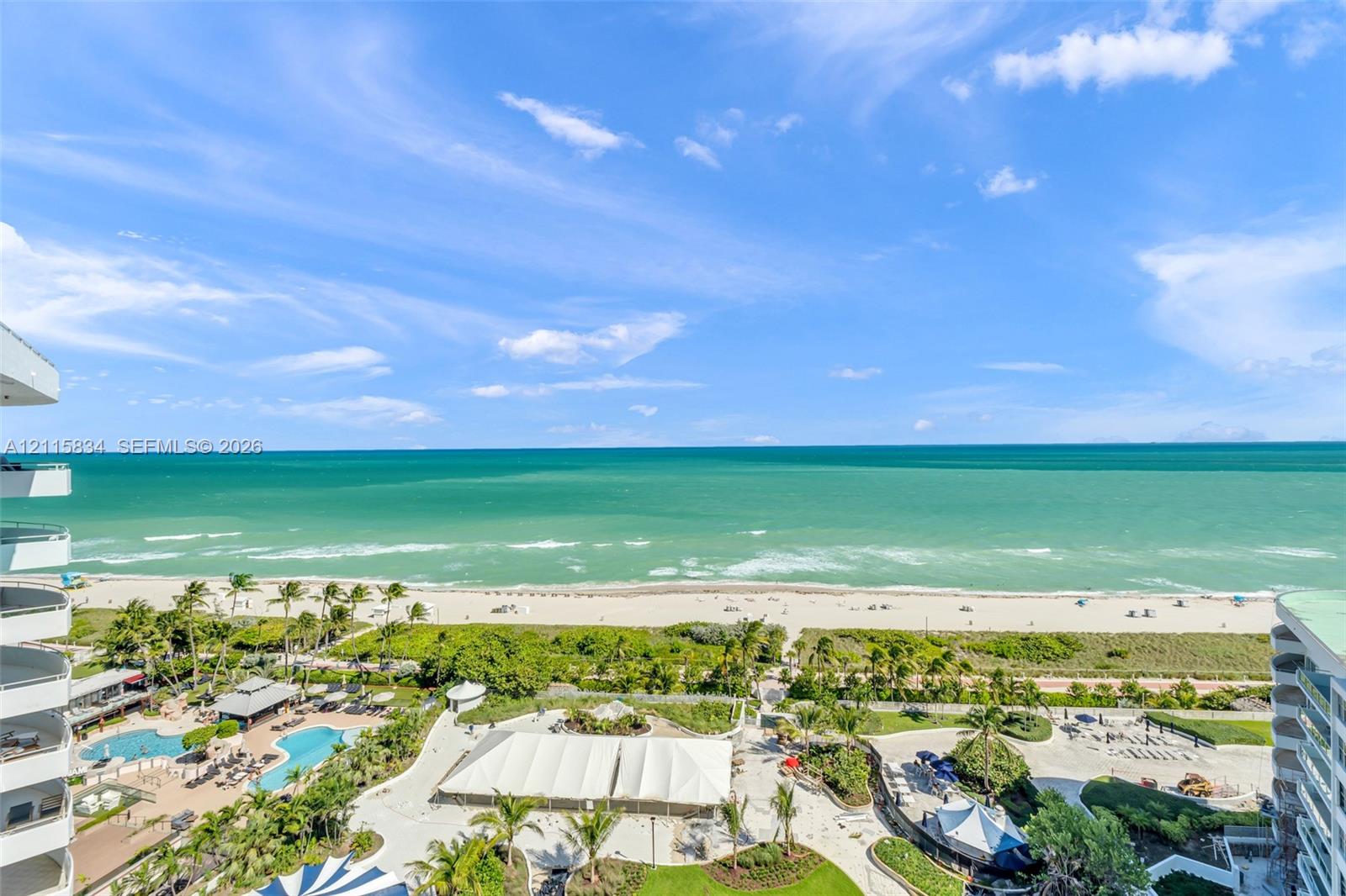 Elevated coastal scenery featuring direct ocean frontage, a sandy beach, and palm-lined grounds with multiple pools