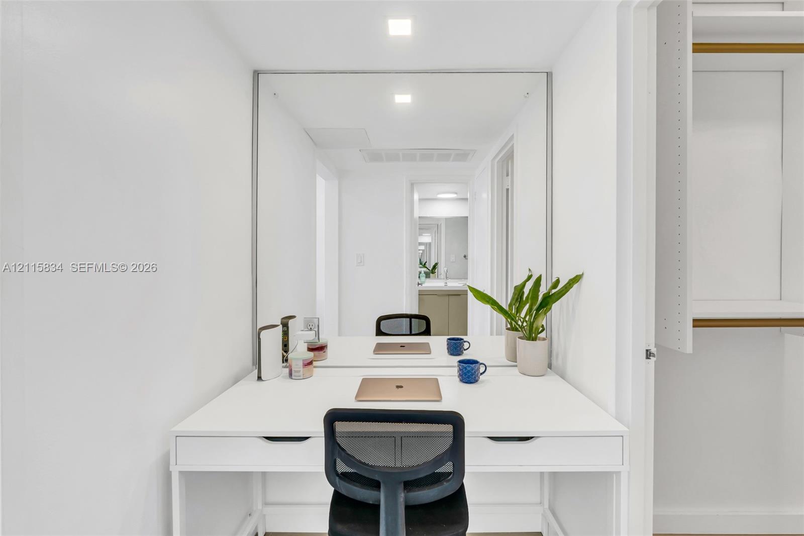 Built-in white desk with integrated dual drawers, expansive wall-mounted mirror, recessed LED lighting, and white shelving units