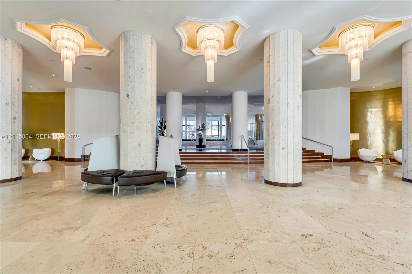 Grand lobby featuring polished stone flooring, towering cylindrical structural columns, multi-tiered tiered tiered pendant lighting, recessed tray ceiling detailing, and metallic wall accents