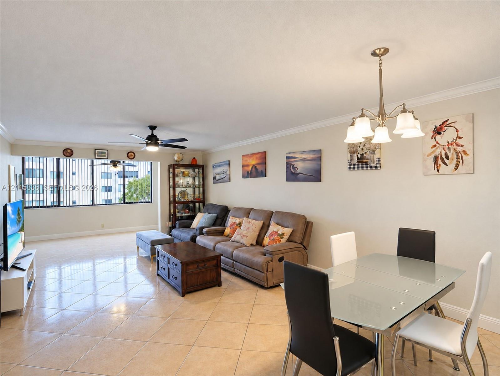Open-concept area featuring light-toned tile flooring, crown molding, a multi-arm chandelier, and floor-to-ceiling windows with vertical blinds