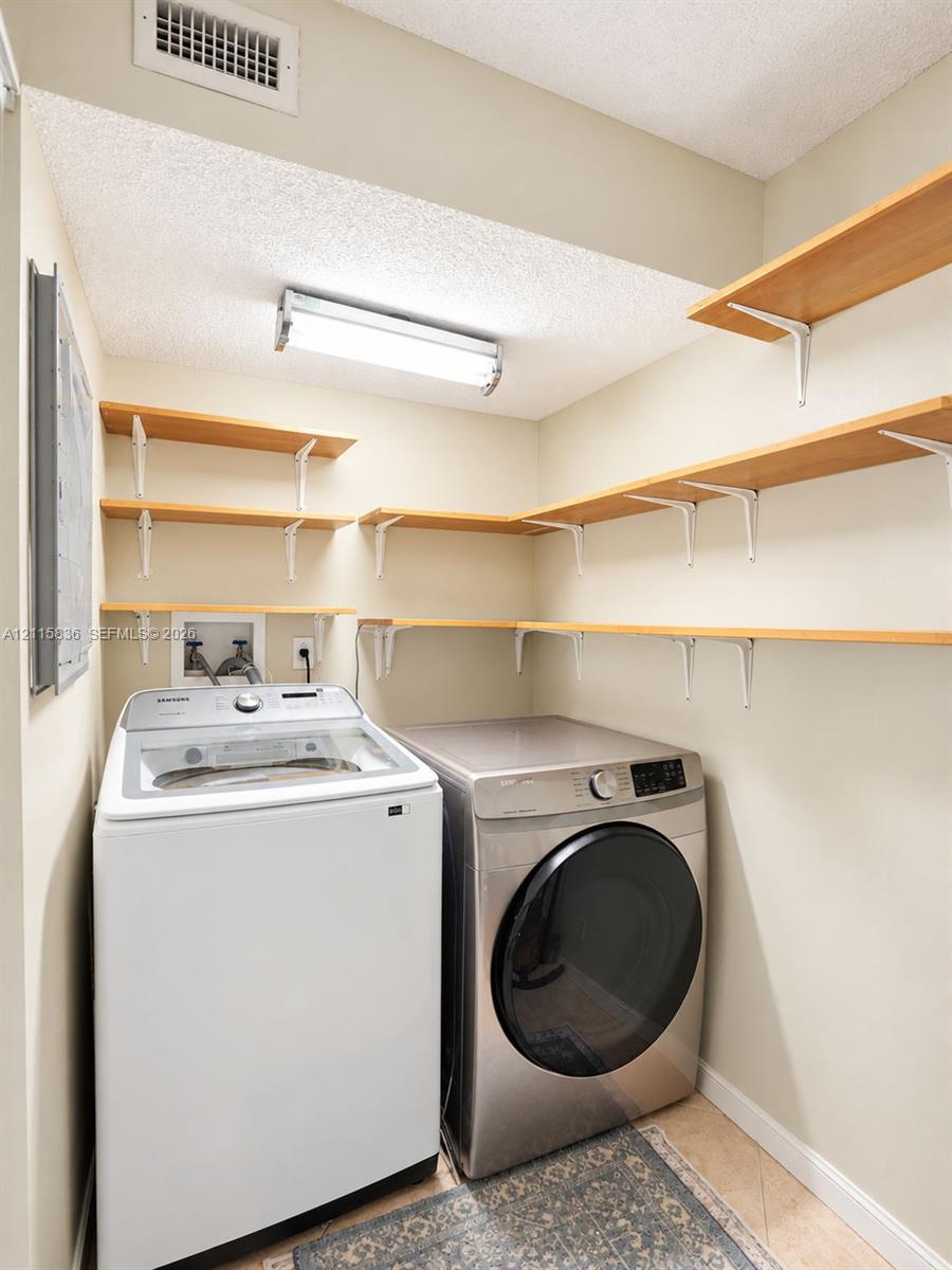 Utility area featuring stainless steel laundry appliances, multi-level wall-mounted shelving, and overhead linear lighting