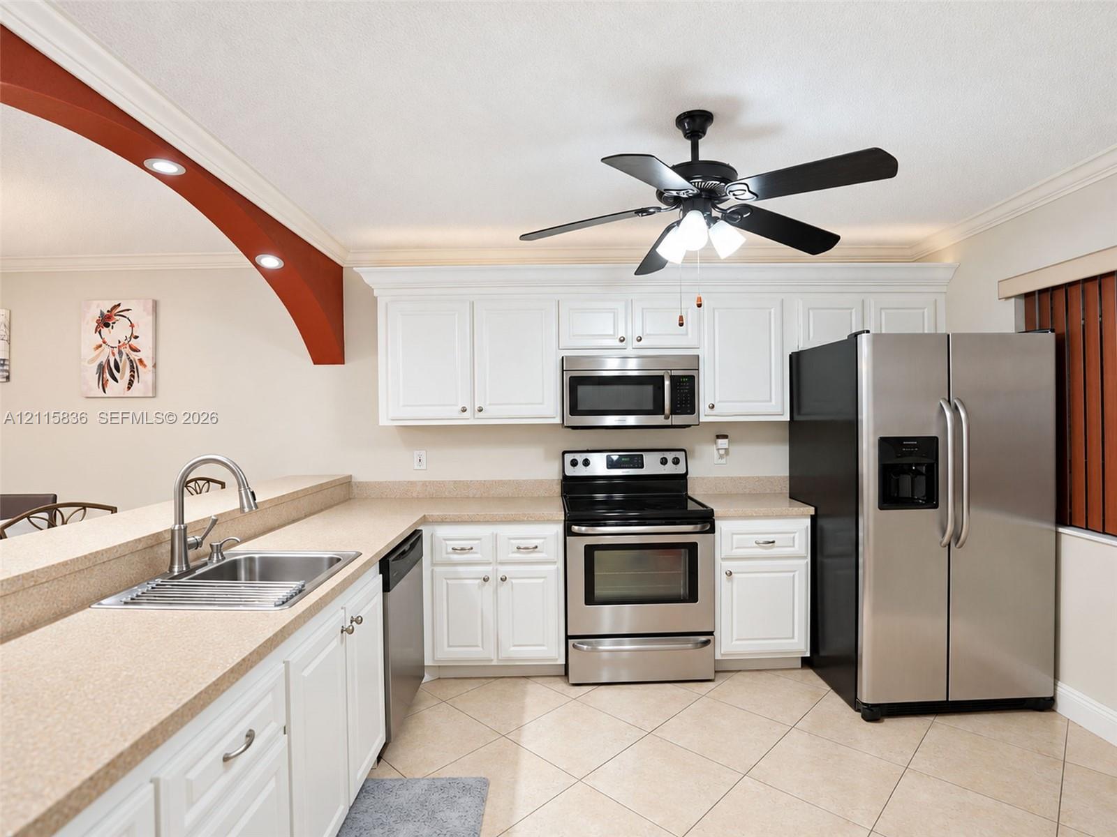 Kitchen featuring white cabinetry, solid-surface countertops, stainless steel appliances, a dual-basin sink with a pull-down faucet, and neutral tile flooring