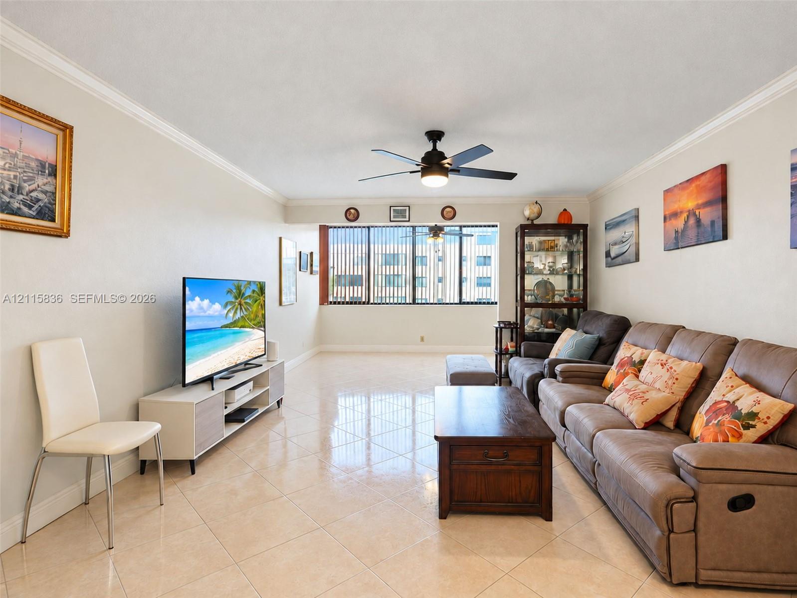 Neutral-toned room featuring large-format tile flooring, crown molding, a central ceiling fan with an integrated light fixture, and floor-to-ceiling windows