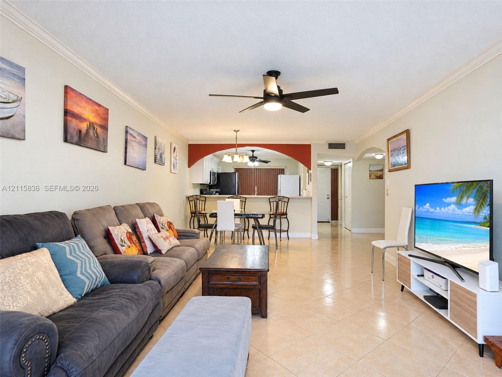Open-concept living space featuring neutral ceramic tile flooring, a prominent decorative archway, recessed lighting, and a multi-blade ceiling fan