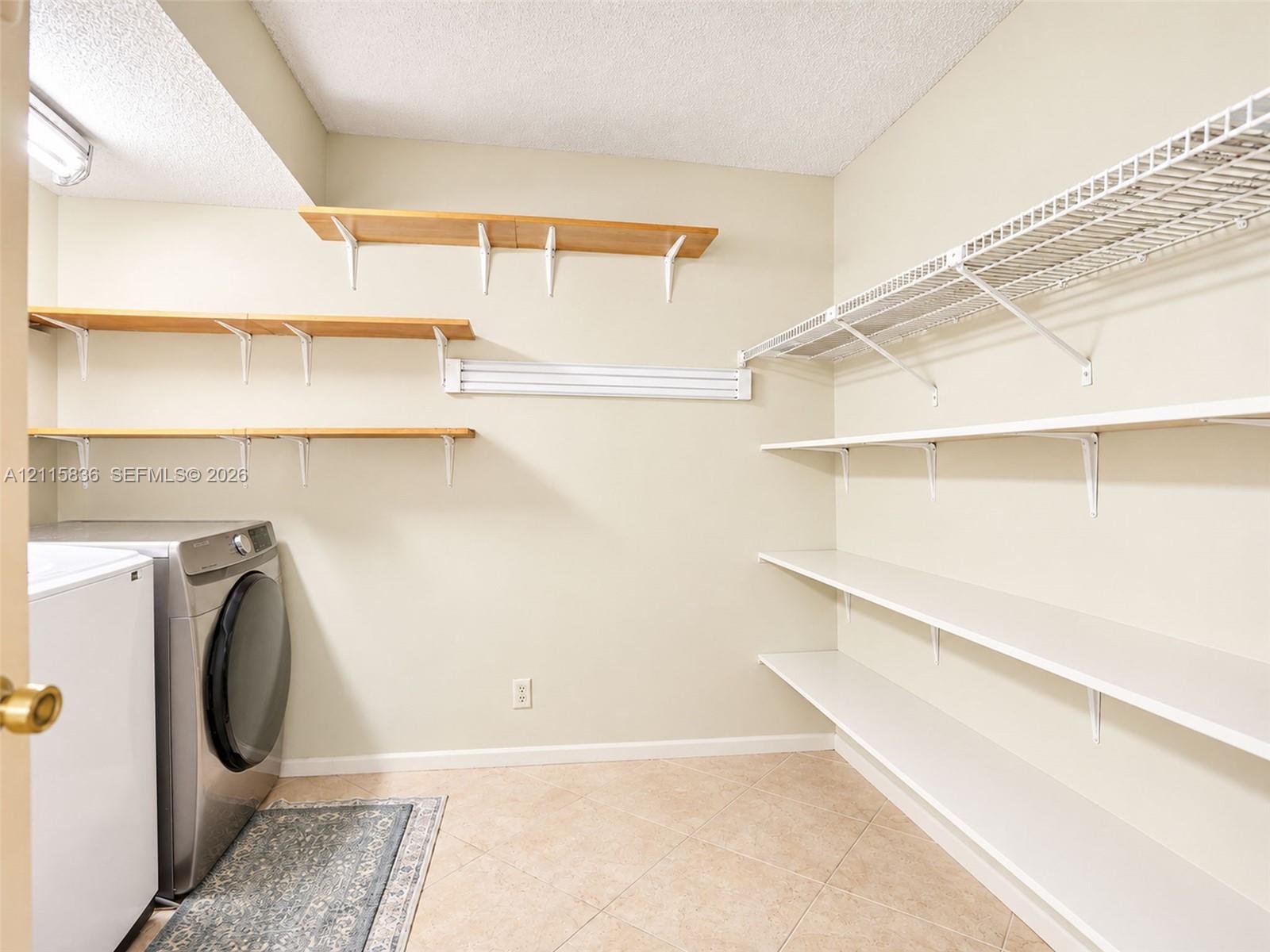 Laundry area featuring tile flooring, three tiers of natural wood-finish wall-mounted shelving, and tiered white wire shelving