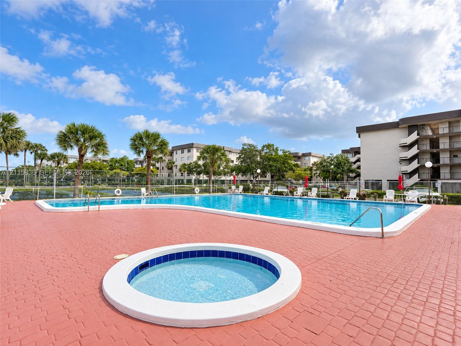 In-ground swimming pool and circular spa with surrounding paver patio, accented by mature palm trees and perimeter fencing