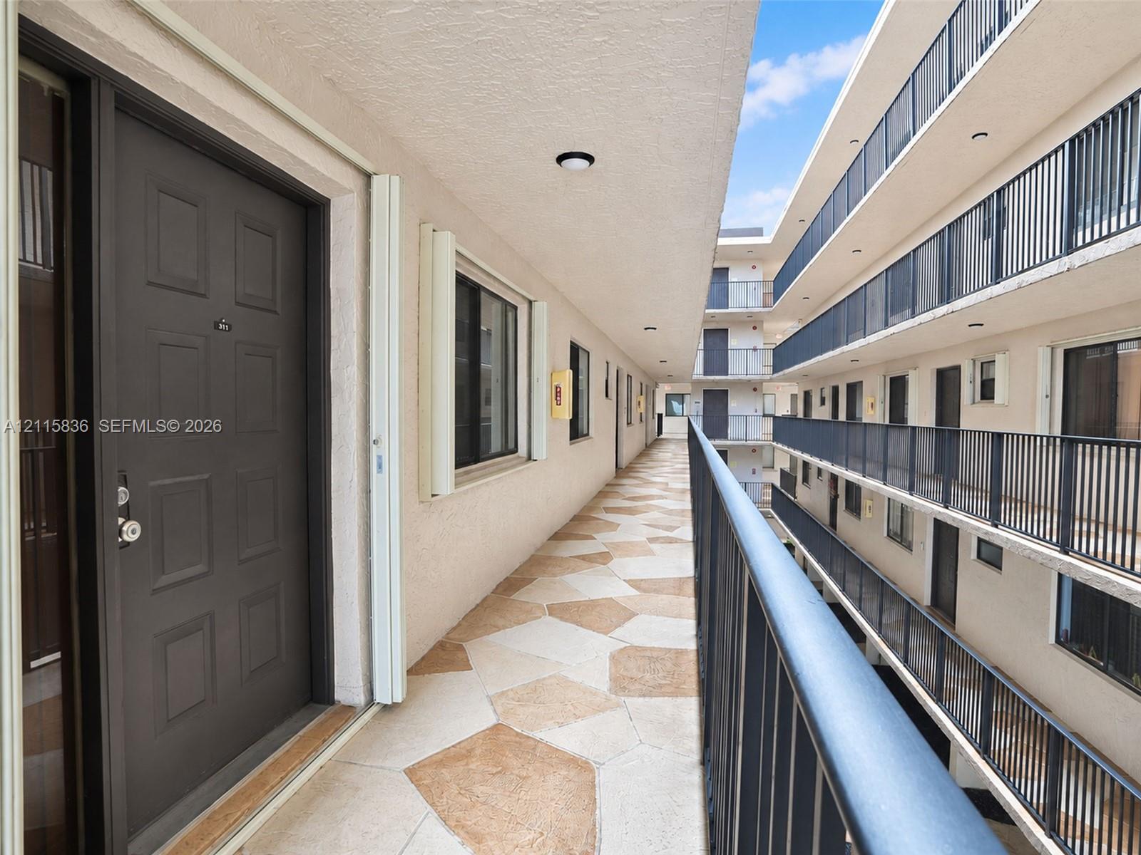 Exterior corridor featuring textured stone-pattern flooring, multi-story metal railings, and recessed ceiling lighting