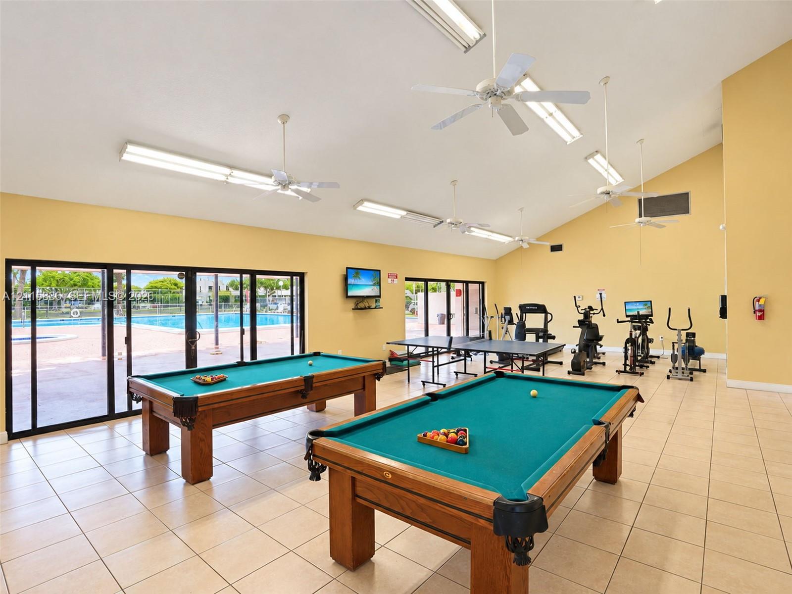 Recreational area featuring ceramic tile flooring, vaulted ceilings with mounted ceiling fans, and expansive sliding glass doors providing outdoor access