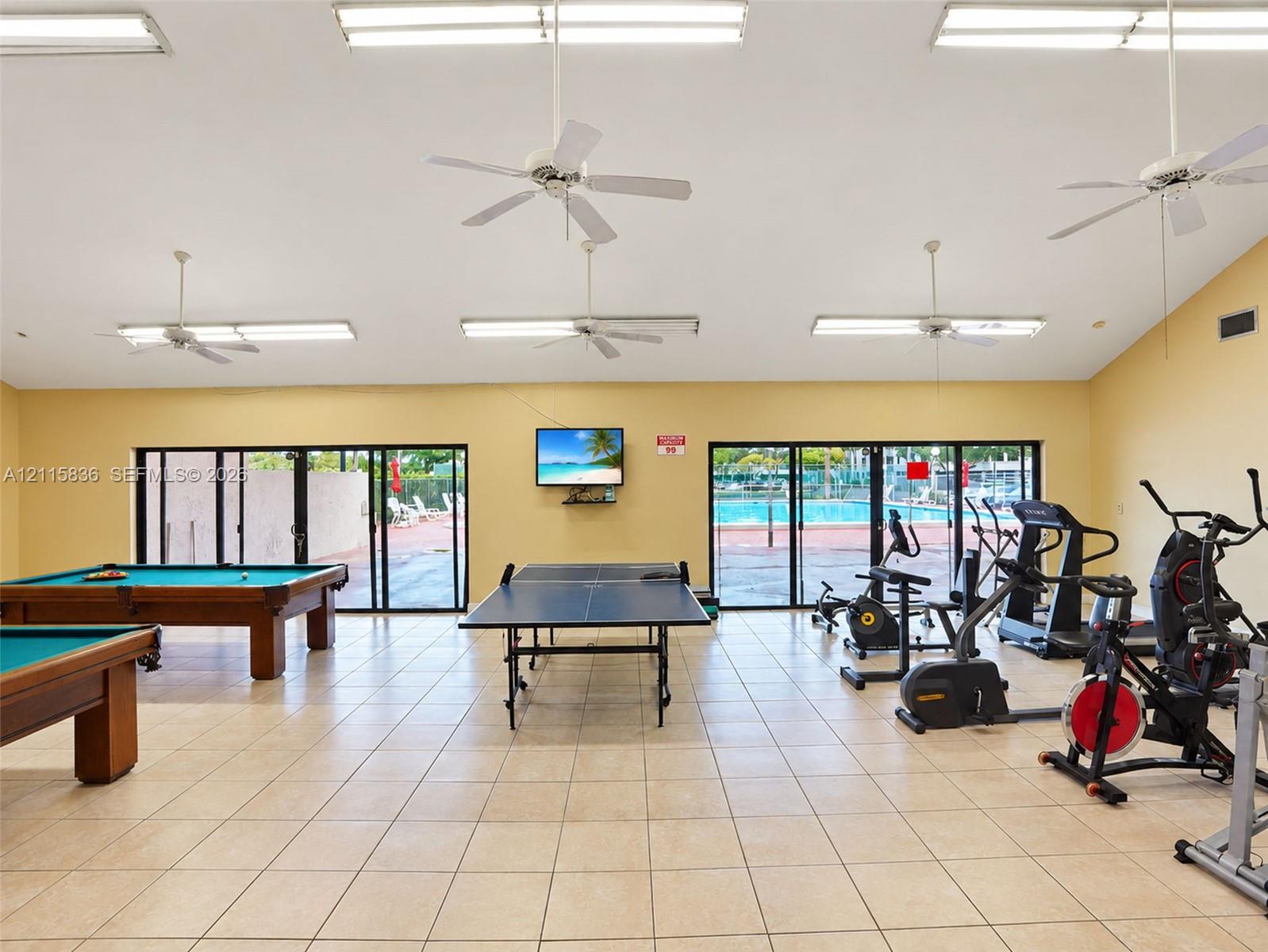 Multi-purpose recreation room featuring ceramic tile flooring, vaulted ceilings with integrated ceiling fans, and floor-to-ceiling glass sliding doors