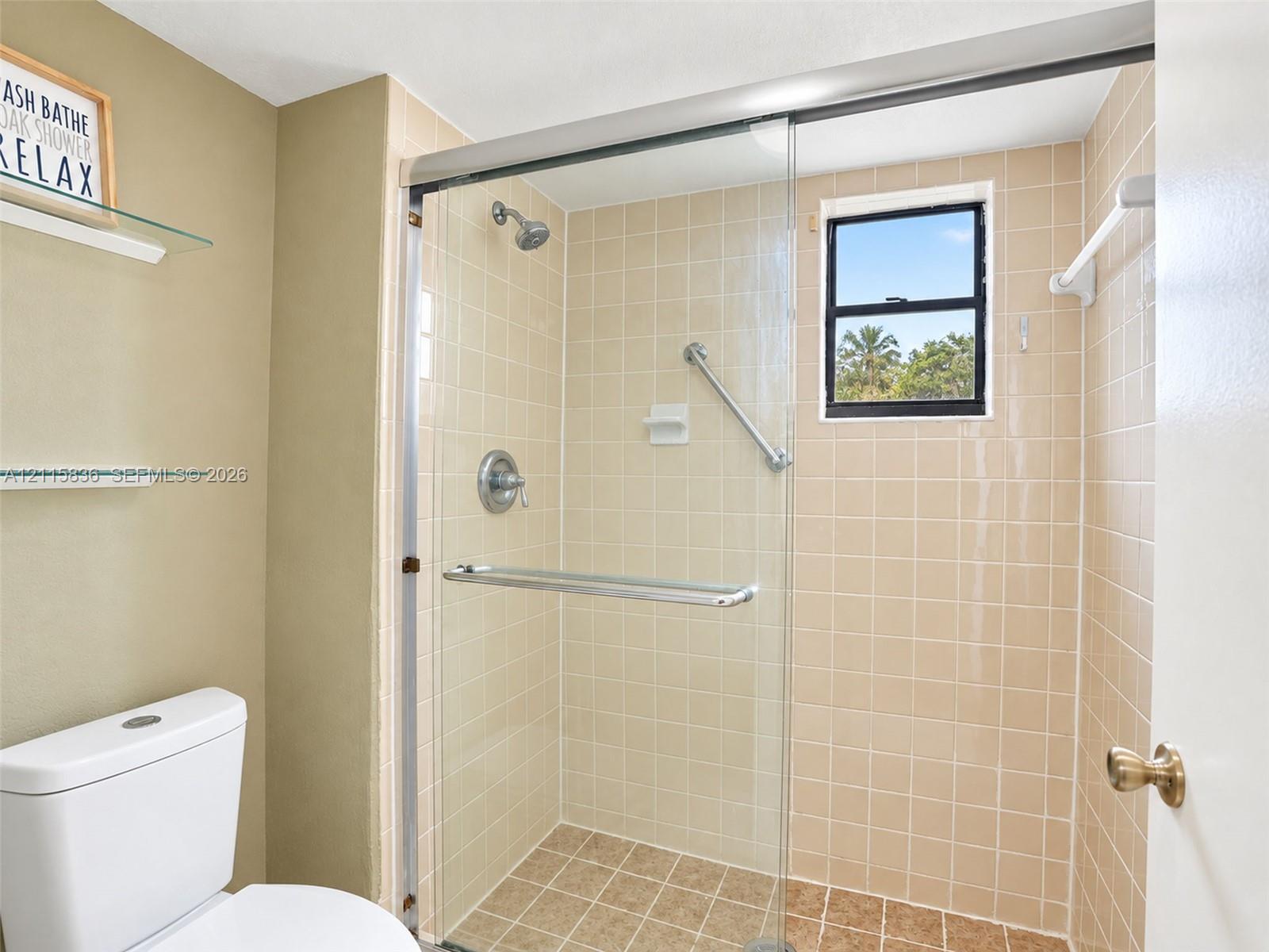 Walk-in shower featuring a sliding glass enclosure, ceramic tile surround, integrated grab bar, and wall-mounted showerhead, accompanied by two built-in glass shelving units