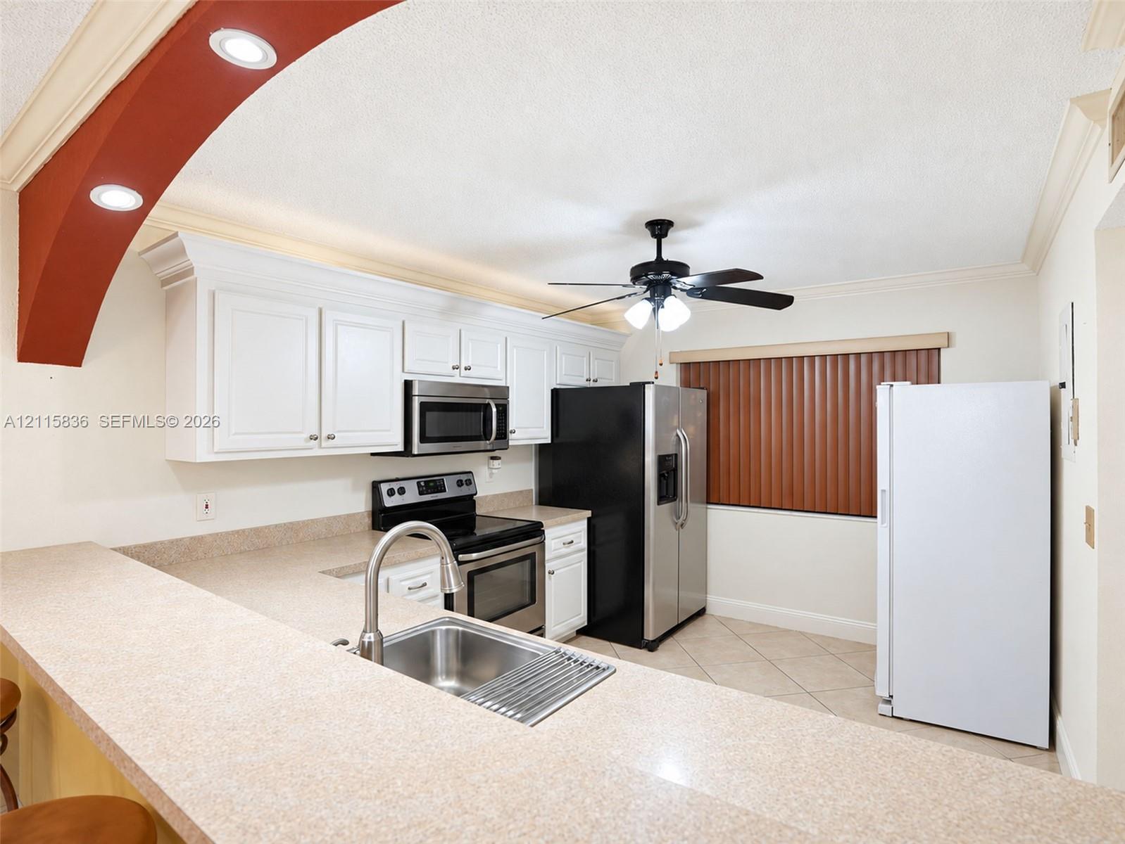 Kitchen featuring white cabinetry, solid-surface countertops, integrated breakfast bar with stainless steel sink, recessed lighting, and an arched architectural detail