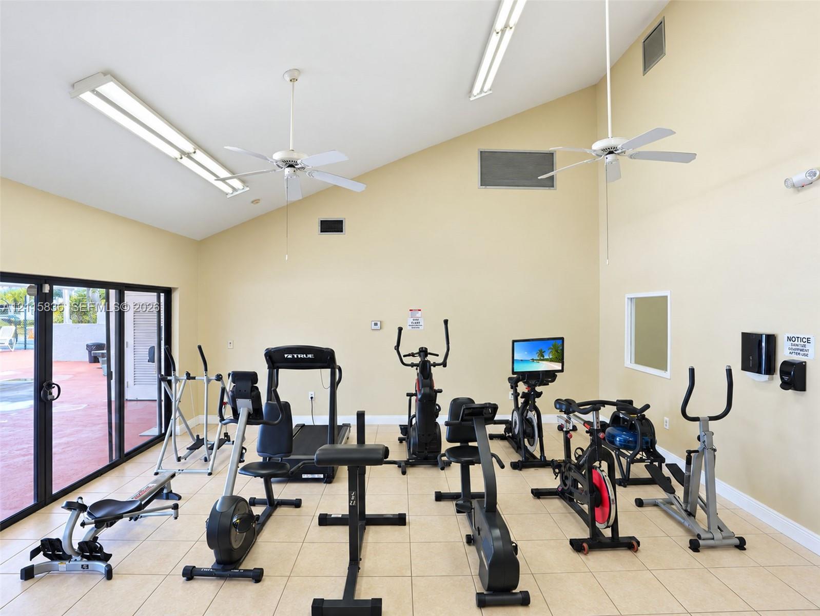 Vaulted ceiling with dual overhead ceiling fans, linear fluorescent lighting, tile flooring, and sliding glass door access