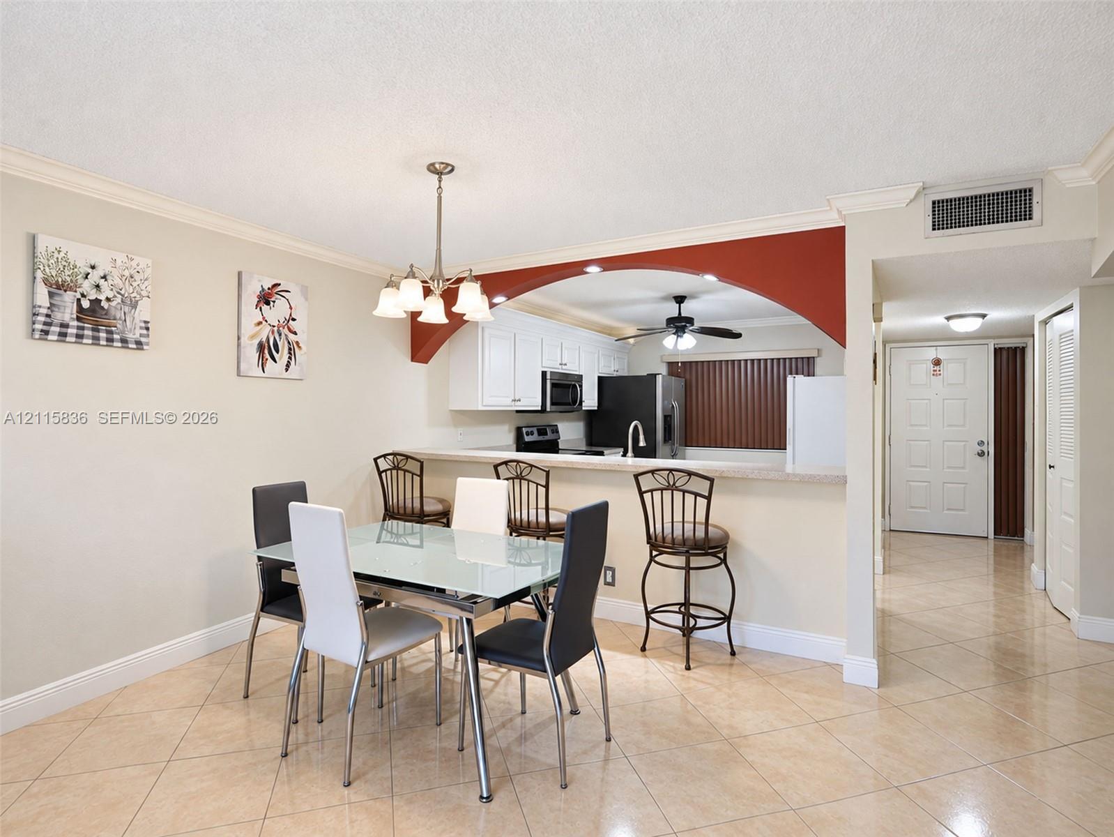 Dining area featuring tile flooring, a decorative chandelier, and a kitchen pass-through with a built-in breakfast bar framed by a rounded archway