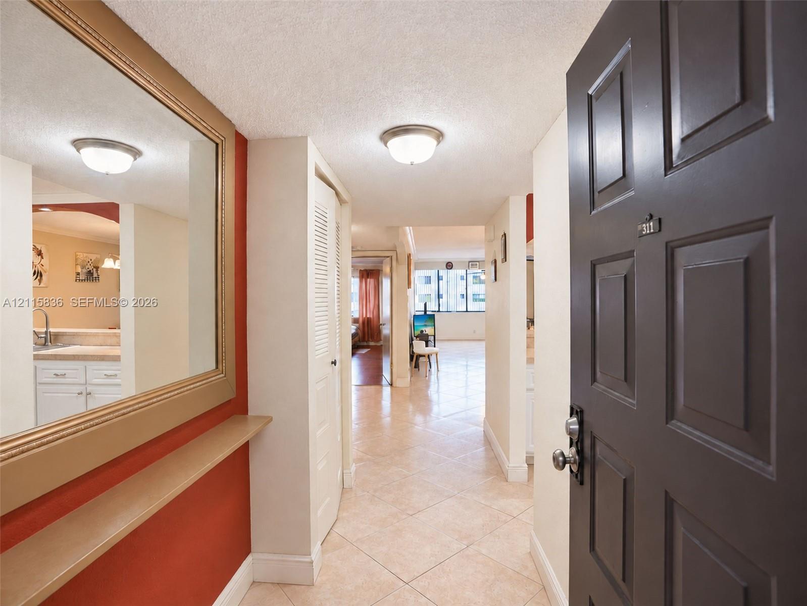 Entryway featuring large wall-mounted mirror, built-in shelving, tiled flooring, louvered closet doors, and flush-mount ceiling lighting
