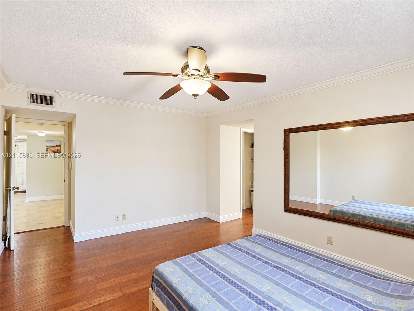 Wood-finish flooring, ceiling fan with integrated lighting, and wall-mounted oversized mirror with a decorative frame