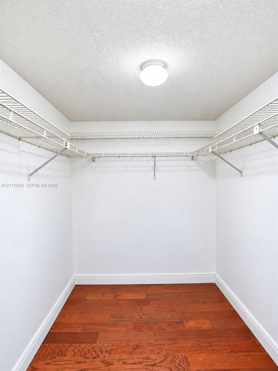 Walk-in closet featuring wood-finish flooring, white walls, and tiered metal wire shelving with an integrated ceiling-mounted light fixture