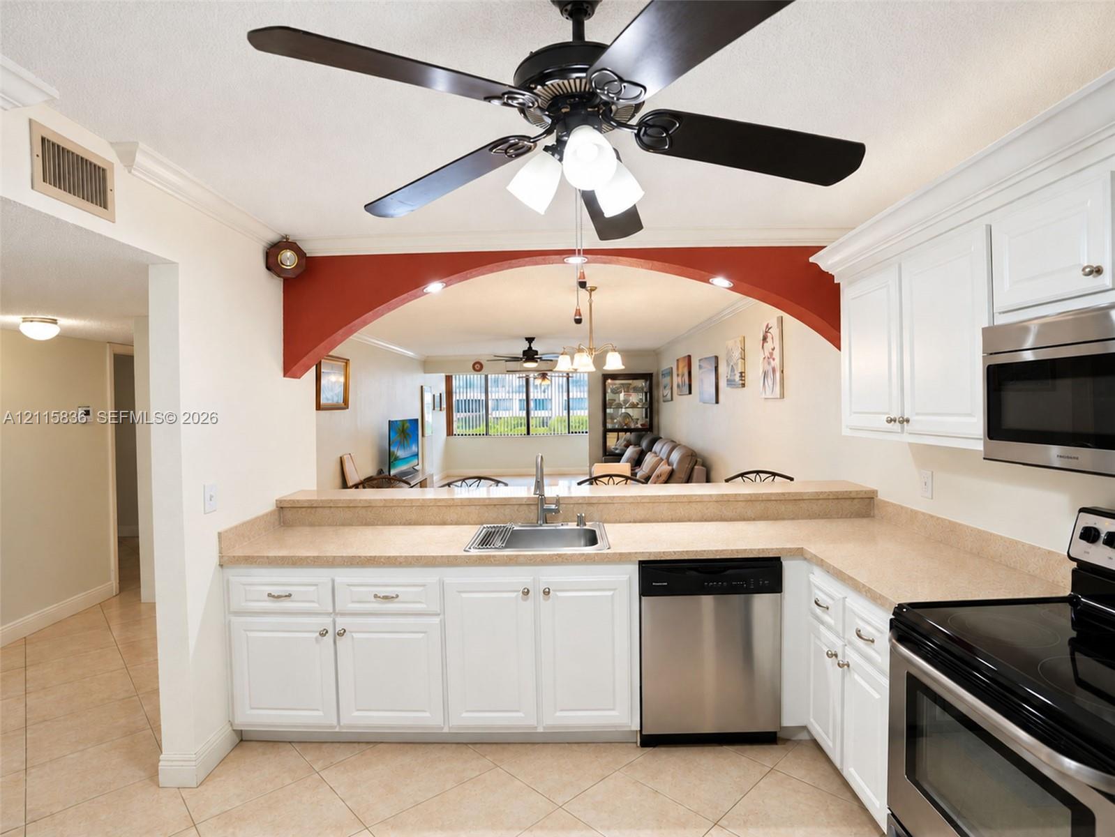 Kitchen featuring white cabinetry, solid-surface countertops, stainless steel appliances, tile flooring, and a decorative arched pass-through opening