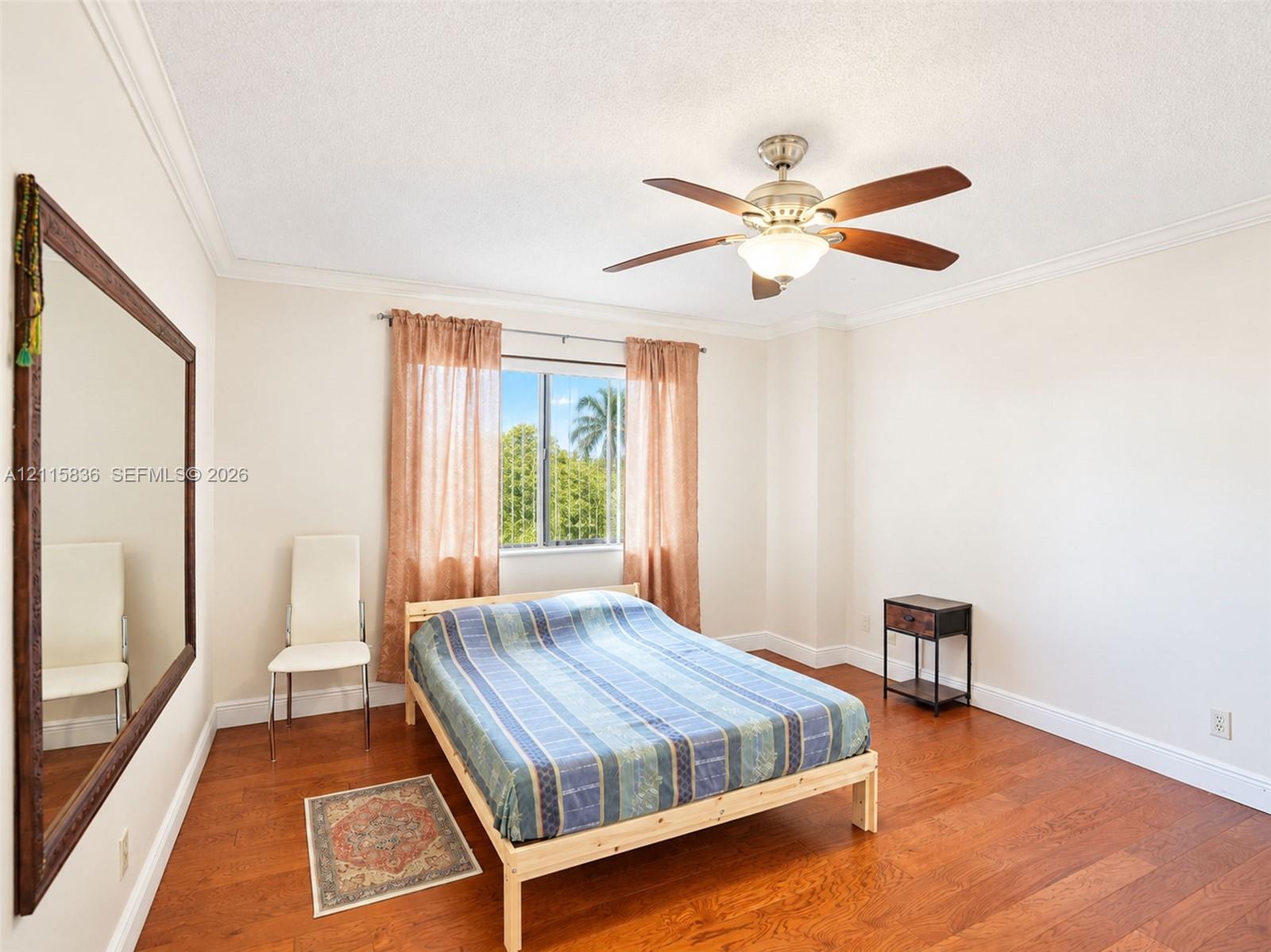 Wood-finish flooring, crown molding, multi-blade ceiling fan with integrated lighting, and a large-format wall mirror with a wood frame