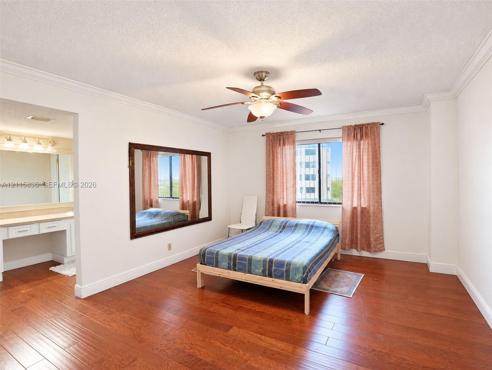 Wood-finish flooring, ceiling fan with integrated lighting, wall-mounted mirror, crown molding, and built-in vanity with countertop