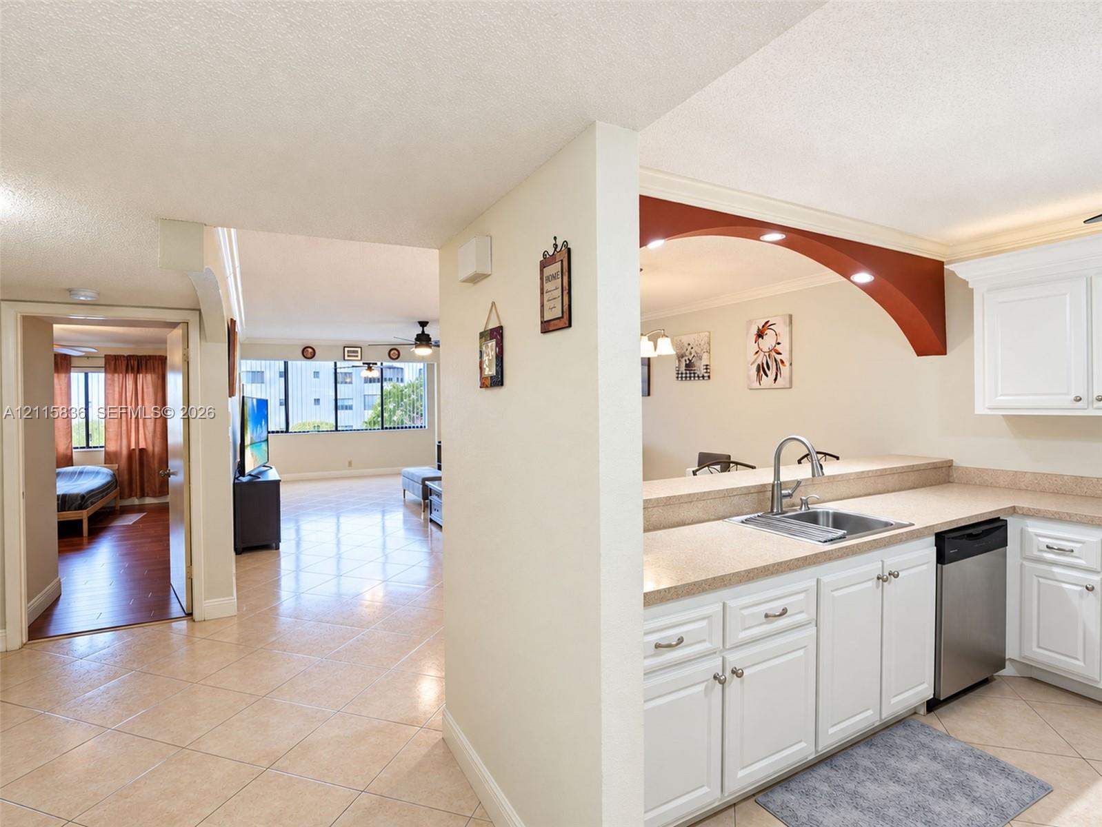 Kitchen featuring white cabinetry, stone-finish countertops, stainless steel sink with arched faucet, and stainless steel dishwasher, with tile flooring throughout