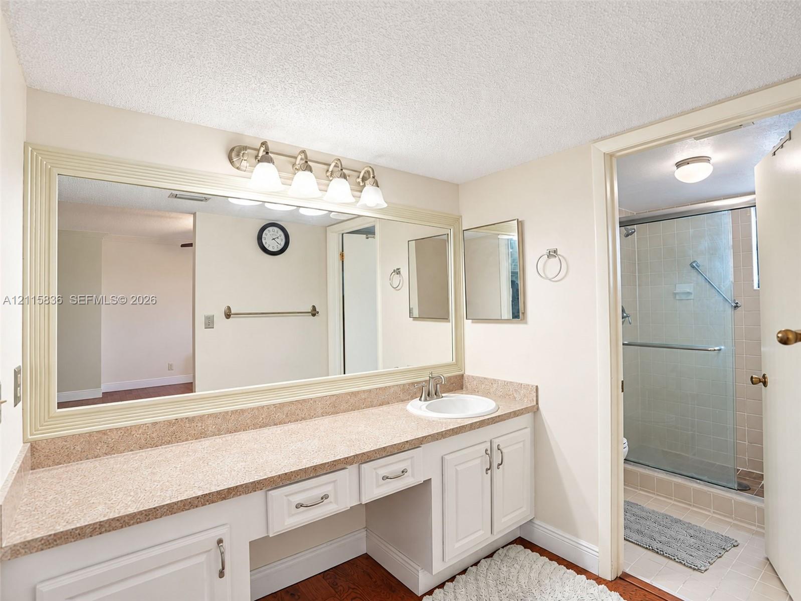 Bathroom featuring a dual-section vanity with a stone-composite countertop, integrated sink, oversized framed mirror, and a walk-in shower enclosure with a glass door