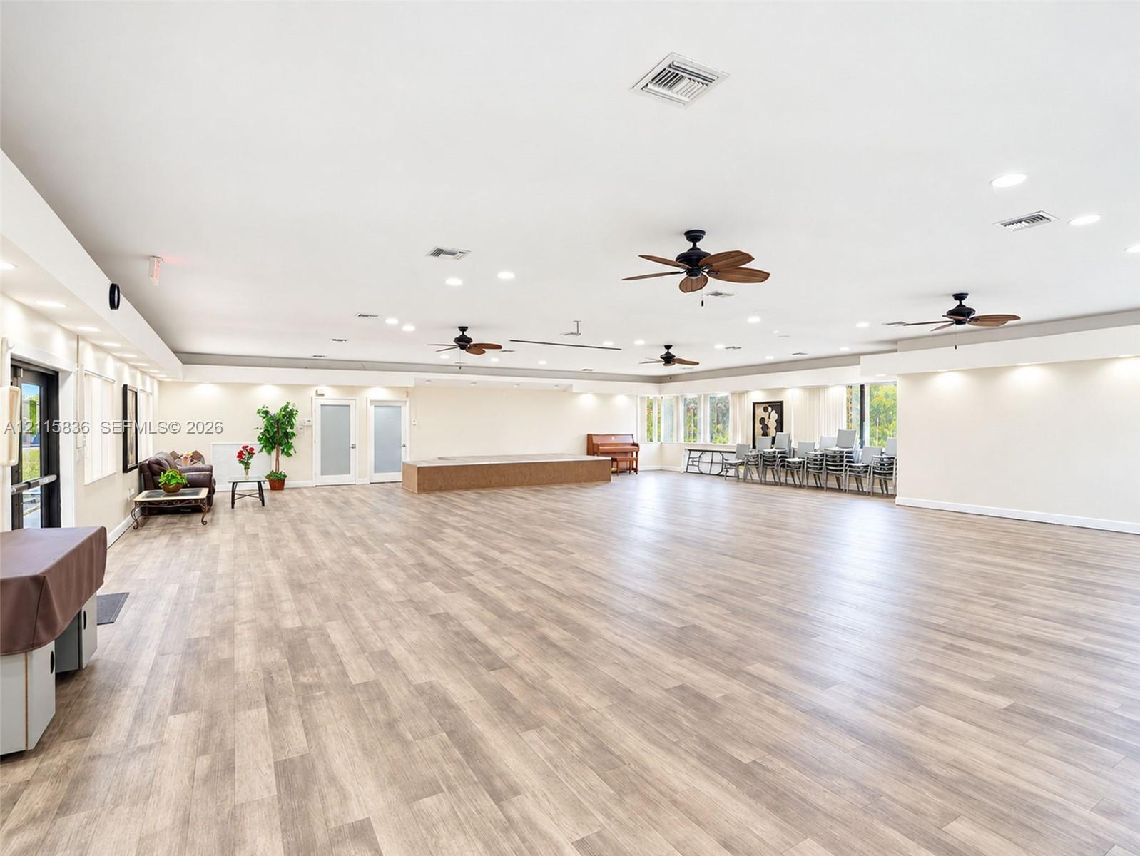 Expansive open-concept interior featuring wood-finish flooring, recessed lighting, multiple ceiling fans, and a raised wooden platform stage