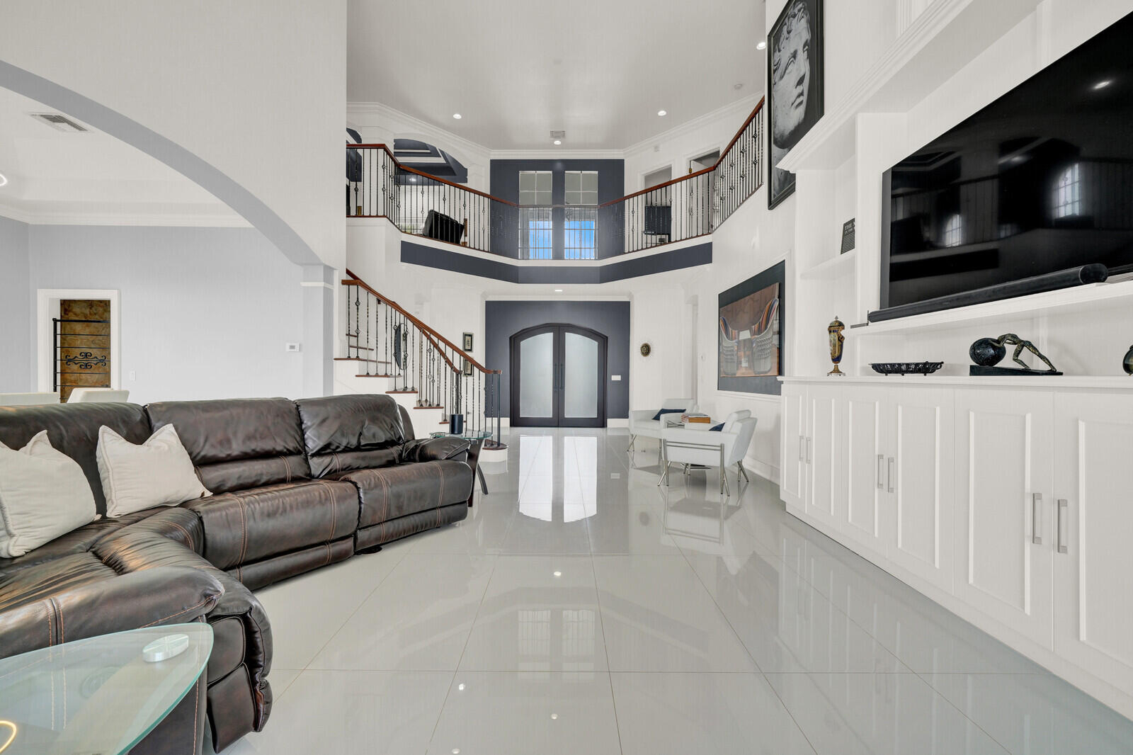Grand foyer featuring a two-story ceiling, a sweeping staircase with a dark wood handrail and wrought iron balusters, and light-toned tile flooring