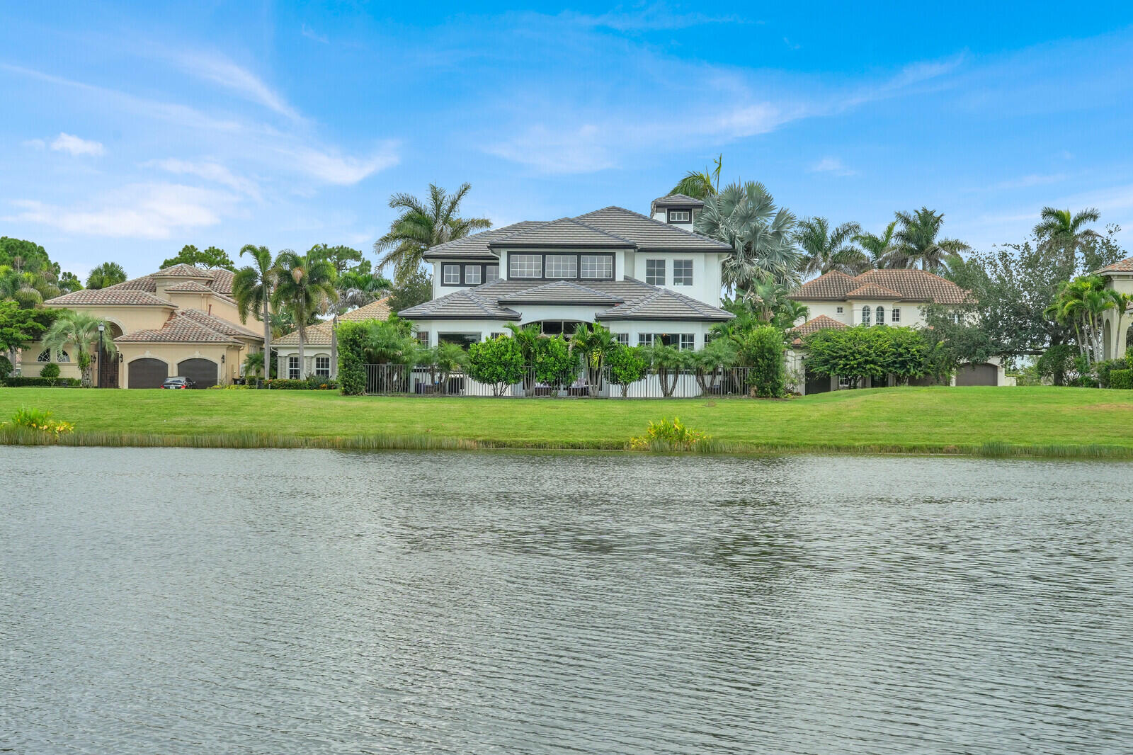 Waterside property featuring a white stucco exterior with dark-framed windows, a multi-level gray tile roof, and a prominent cupola