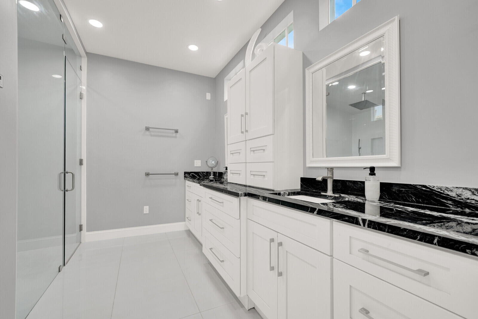 Spacious bathroom featuring a glass-enclosed shower, dual vanity with white cabinetry, polished nickel hardware, and dark stone countertops