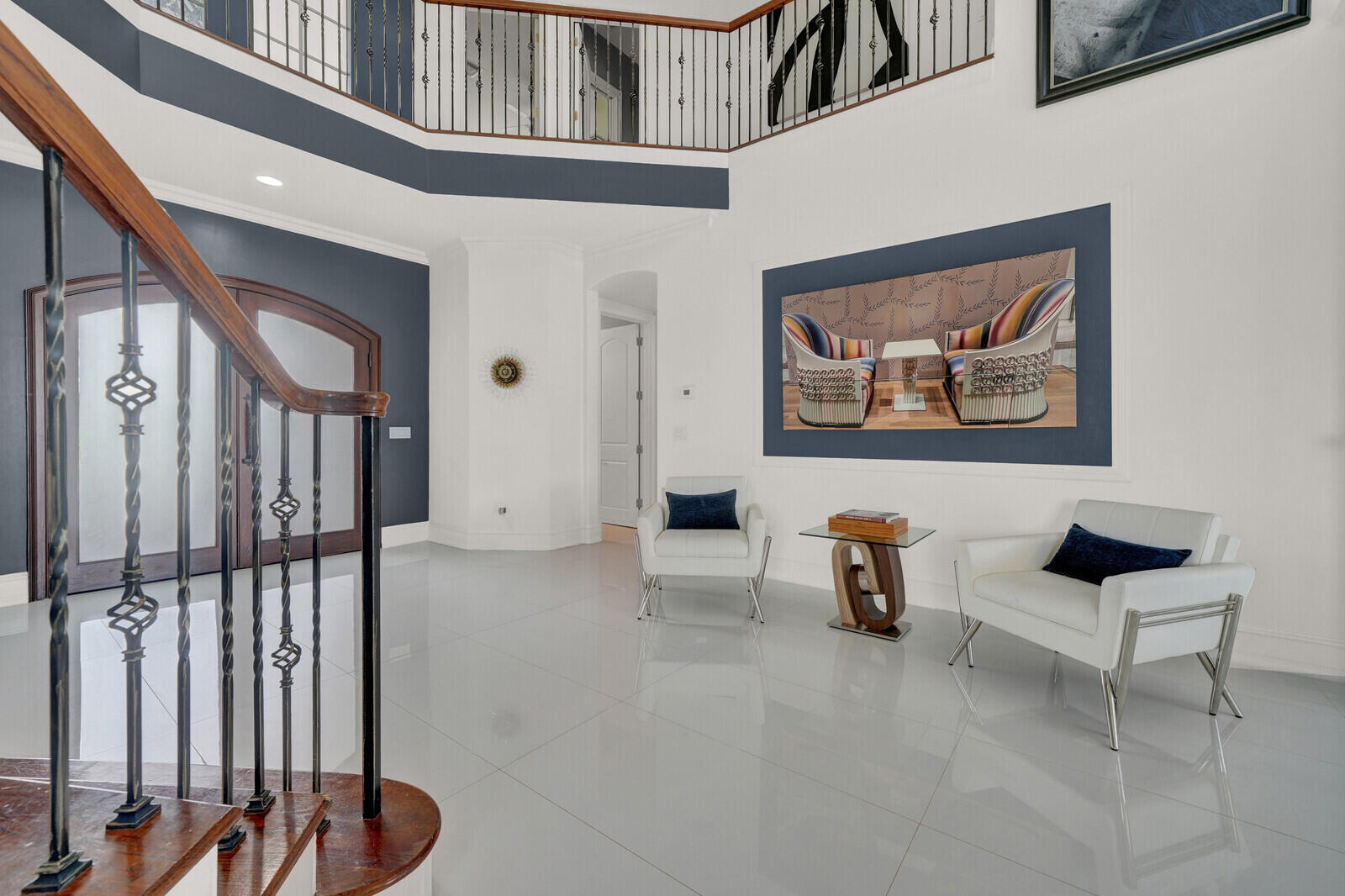 Two-story foyer featuring a grand staircase with wood-finish handrails and wrought iron balusters, light-toned tile flooring, and arched entryway doors