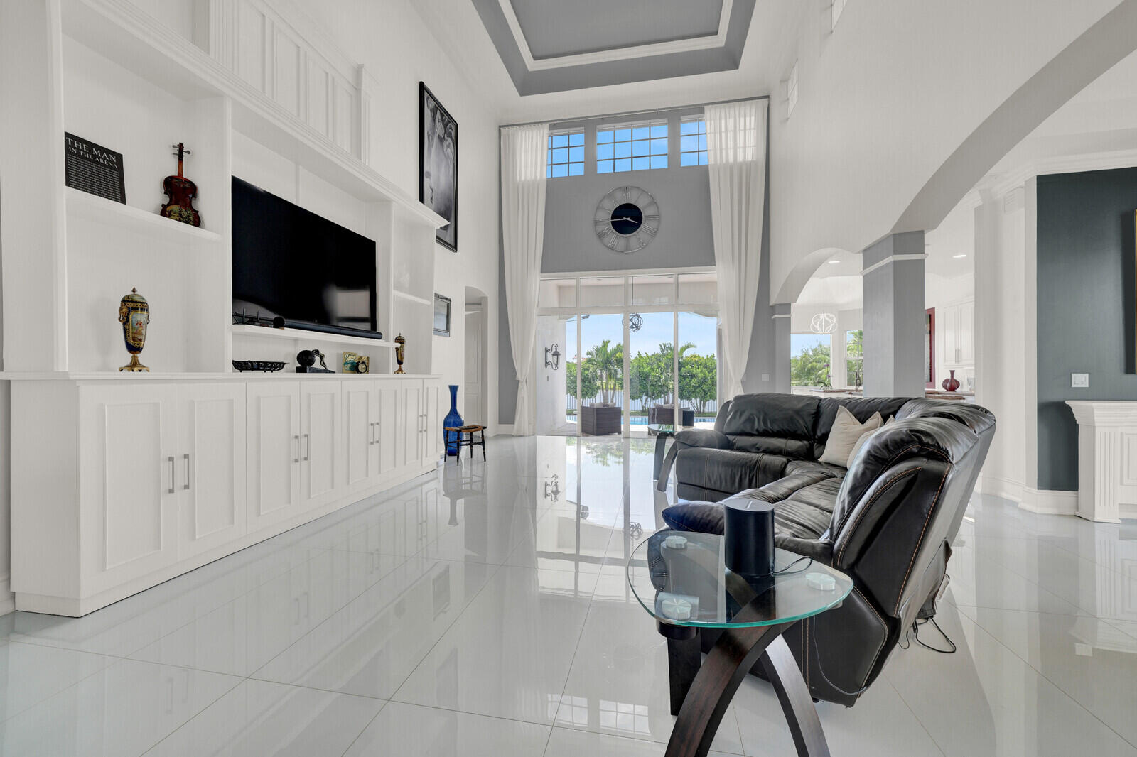 Spacious interior featuring a built-in entertainment center, high ceilings, large format tile flooring, a tiered tray ceiling, and expansive glass doors opening to the exterior