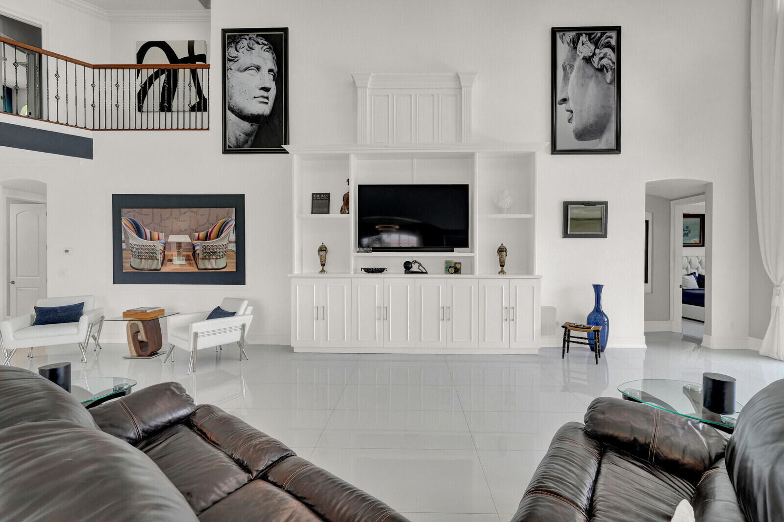 Two-story living area featuring a built-in entertainment center, high ceilings, a second-story landing with wrought iron railing, and reflective tile flooring