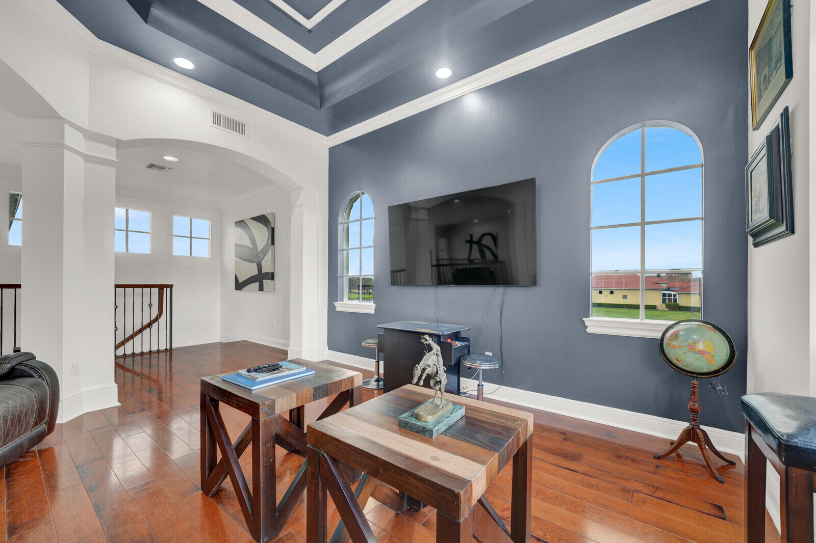 Spacious living area featuring a tray ceiling with accent color, hardwood flooring, arched windows, and a multi-level architectural design with open archways