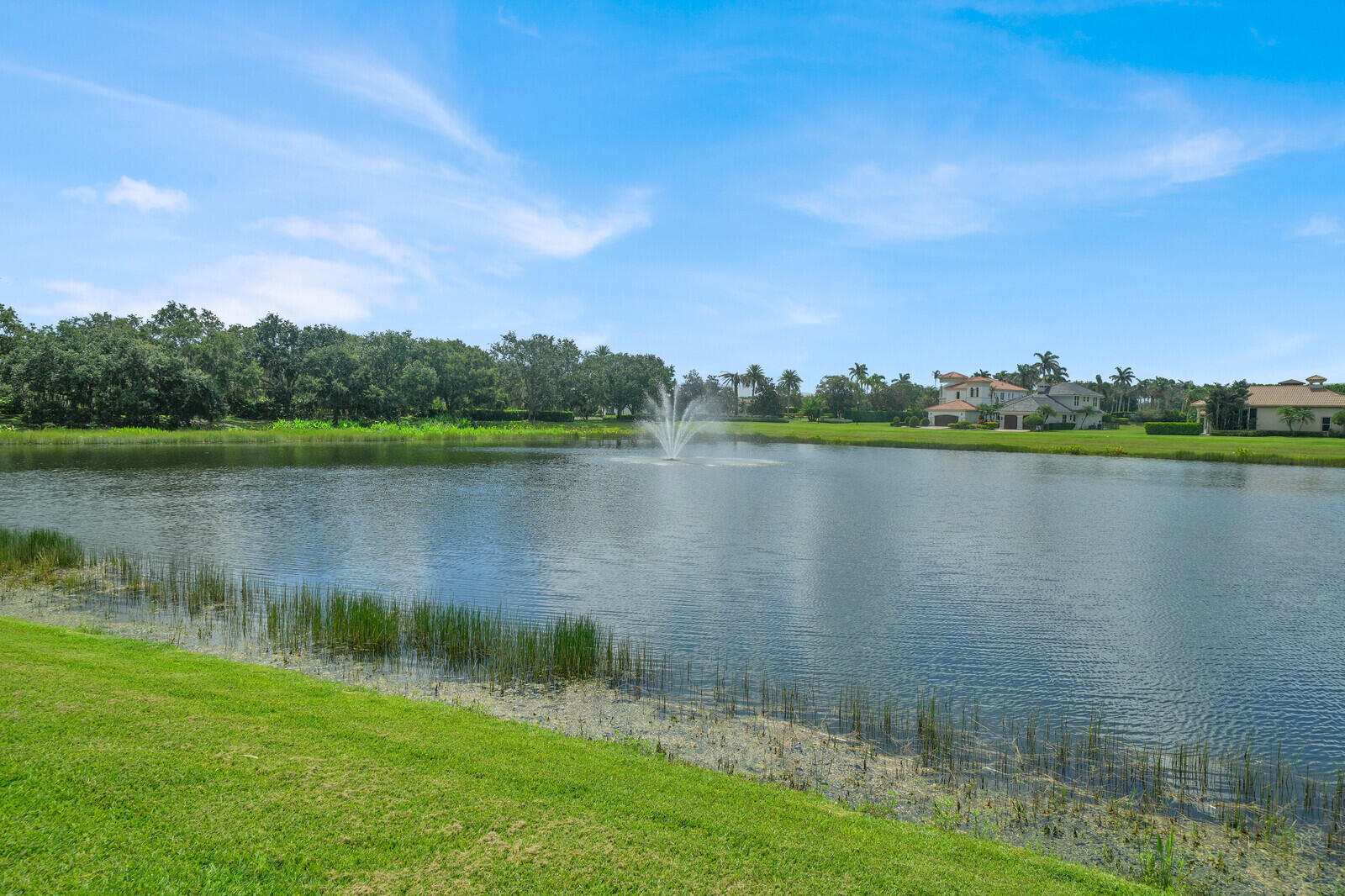 Expansive water feature with a central fountain, bordered by a green lawn and mature trees