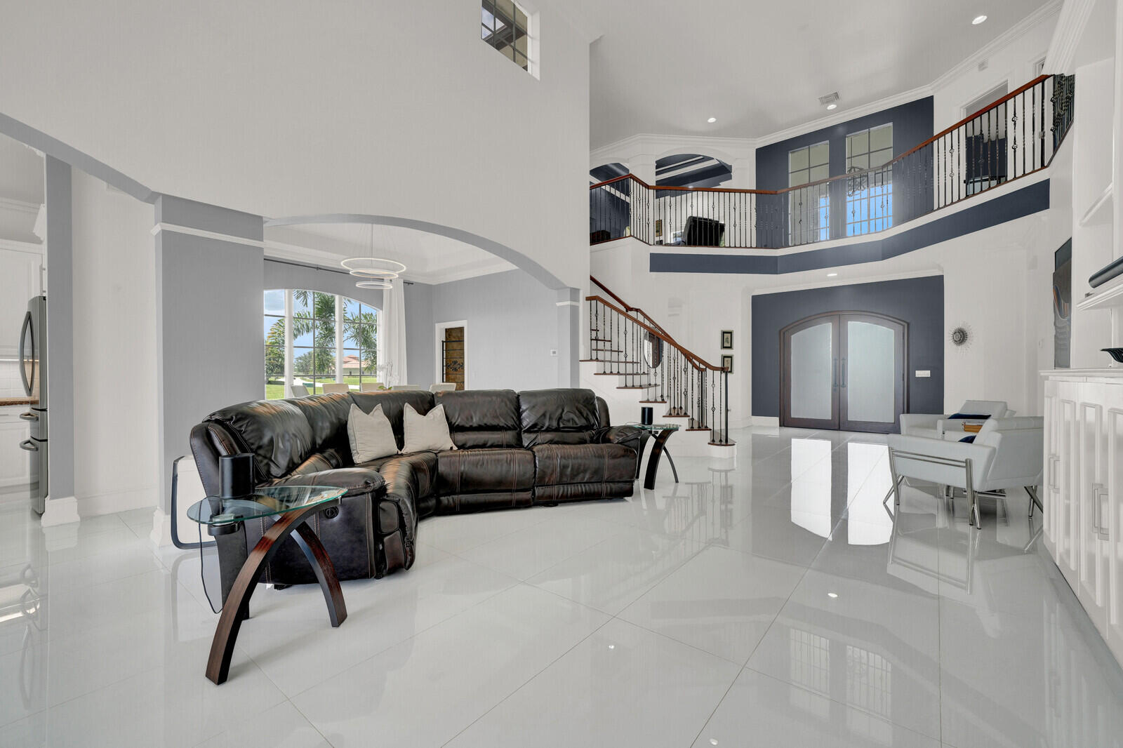 Two-story living area featuring polished porcelain tile flooring, a prominent curved staircase with wood railing and wrought iron balusters, and a second-story interior balcony