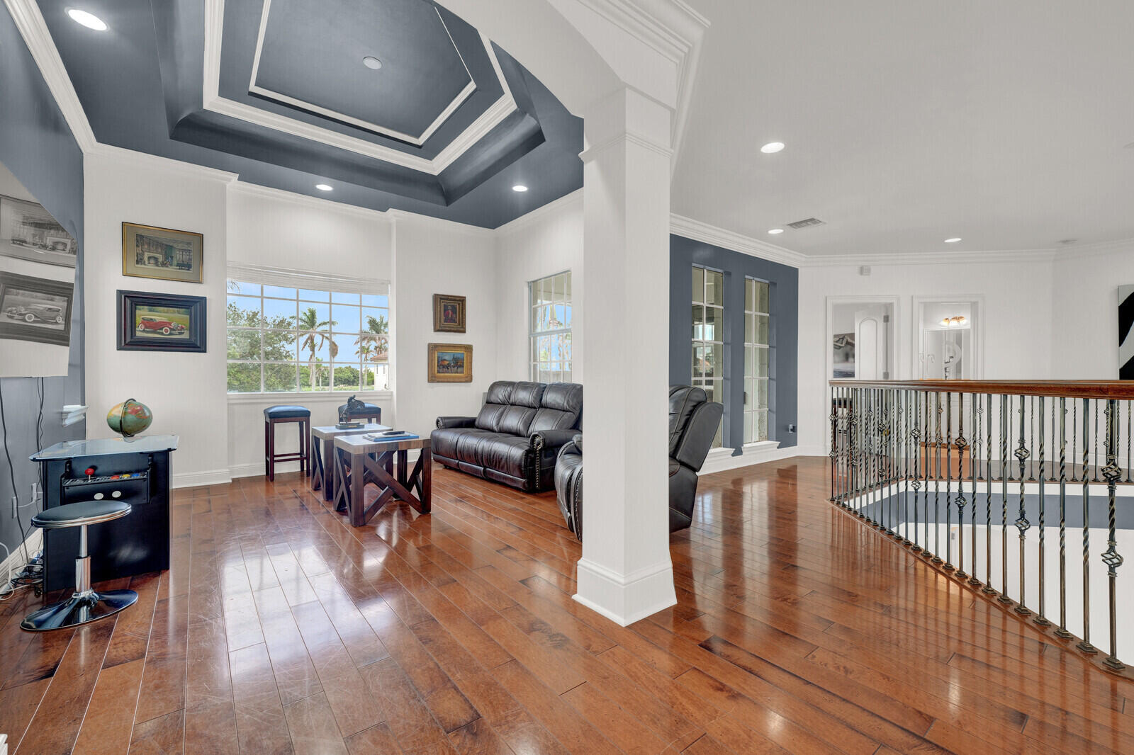 Upper-level living area featuring rich wood-finish flooring, a tray ceiling with recessed lighting, and a large window overlooking tropical foliage