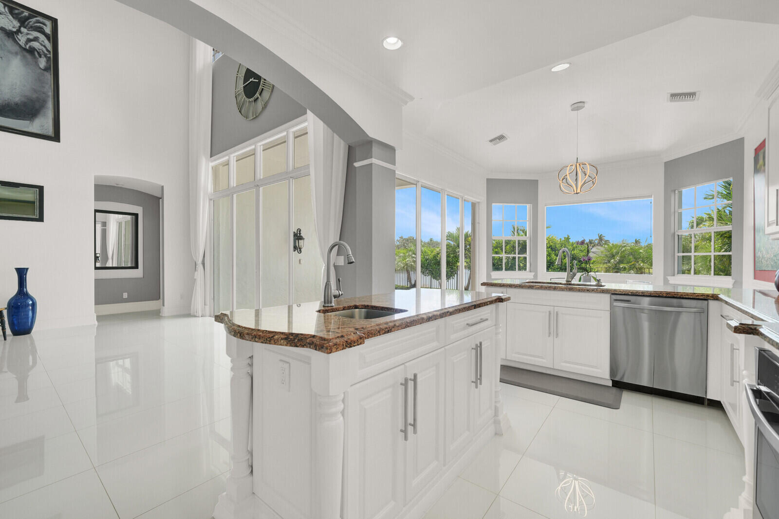 Spacious kitchen featuring an island with a built-in sink, white cabinetry with brushed nickel hardware, stainless steel appliances, and large windows offering abundant natural light
