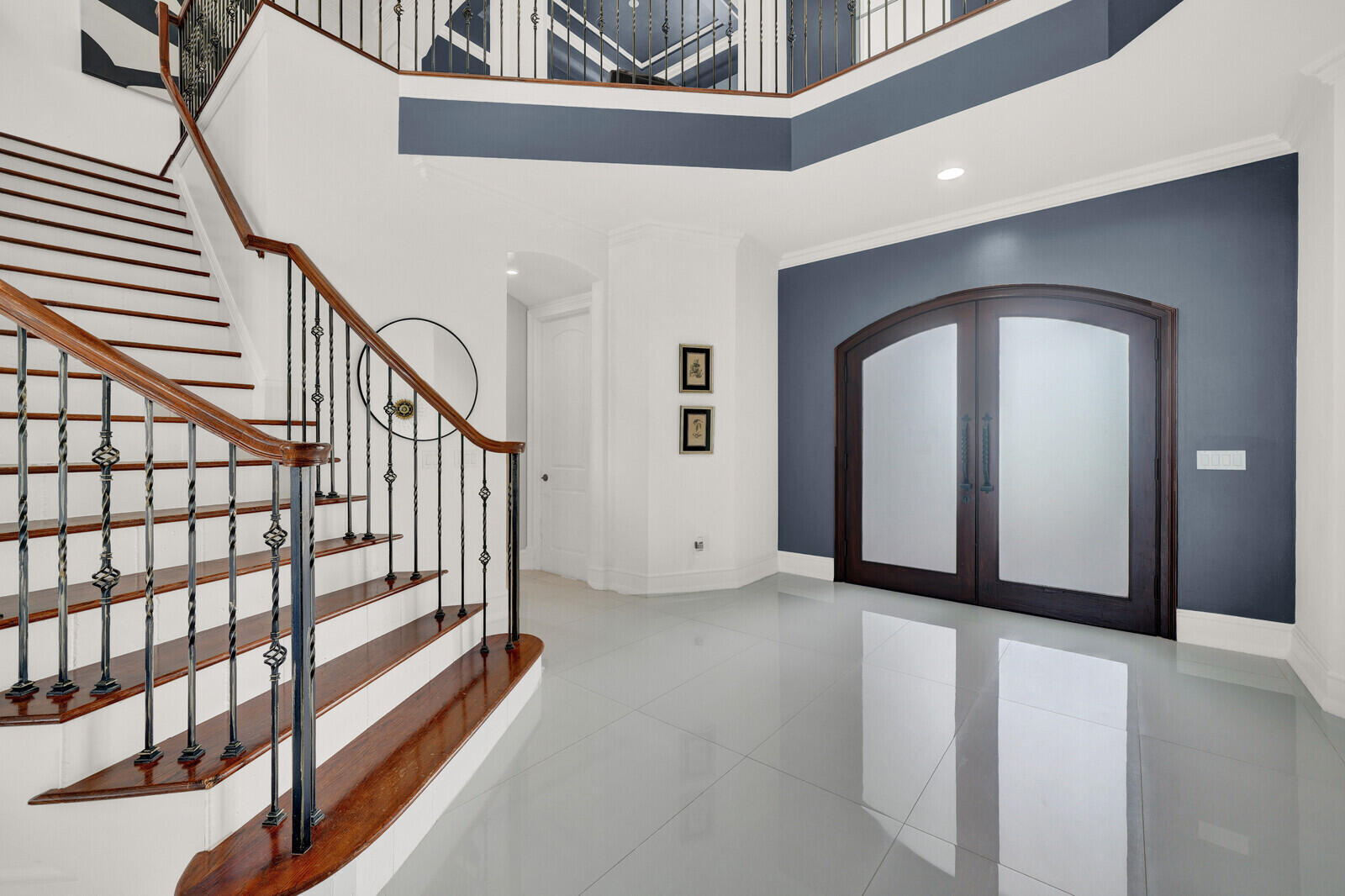 Grand entryway featuring a curved staircase with wrought iron balusters and wood handrails, large format tile flooring, and double arched doors