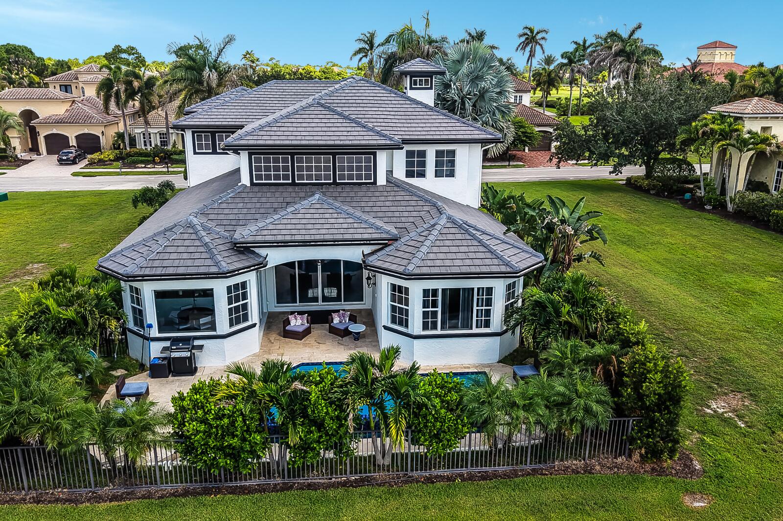 Rear exterior featuring a paver patio with a swimming pool, surrounded by lush landscaping and a perimeter fence