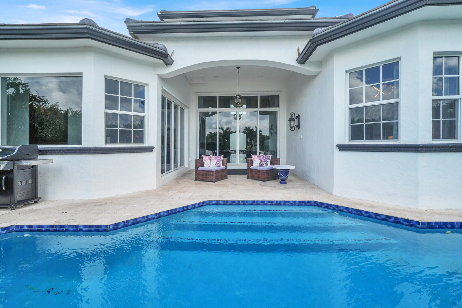 Outdoor living area featuring a blue-tiled swimming pool with integrated steps, a paver patio, and multiple large windows