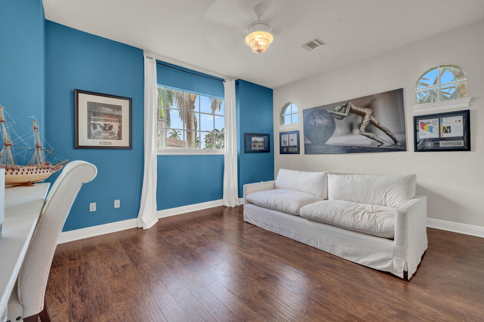 Room featuring wood-finish flooring, a prominent window, two arched transom windows, and a ceiling fan with integrated lighting