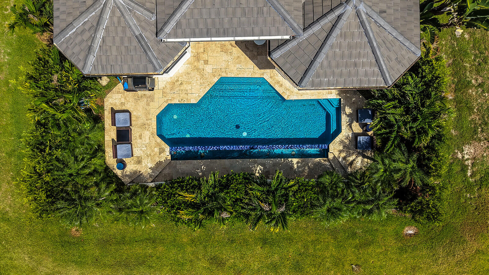 Resort-style pool with integrated steps, surrounded by a stone patio and mature landscaping, all within a large grassy area