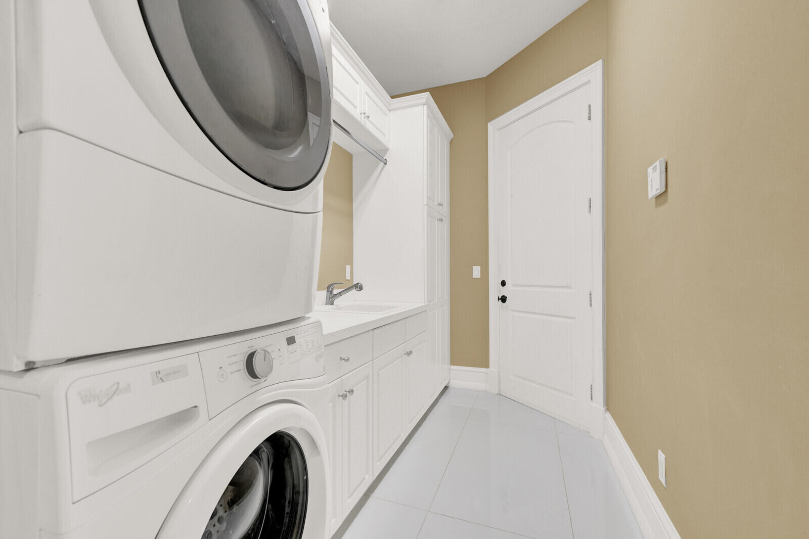 Dedicated utility space featuring a stacked laundry system, extensive white cabinetry, a built-in sink, and light tile flooring