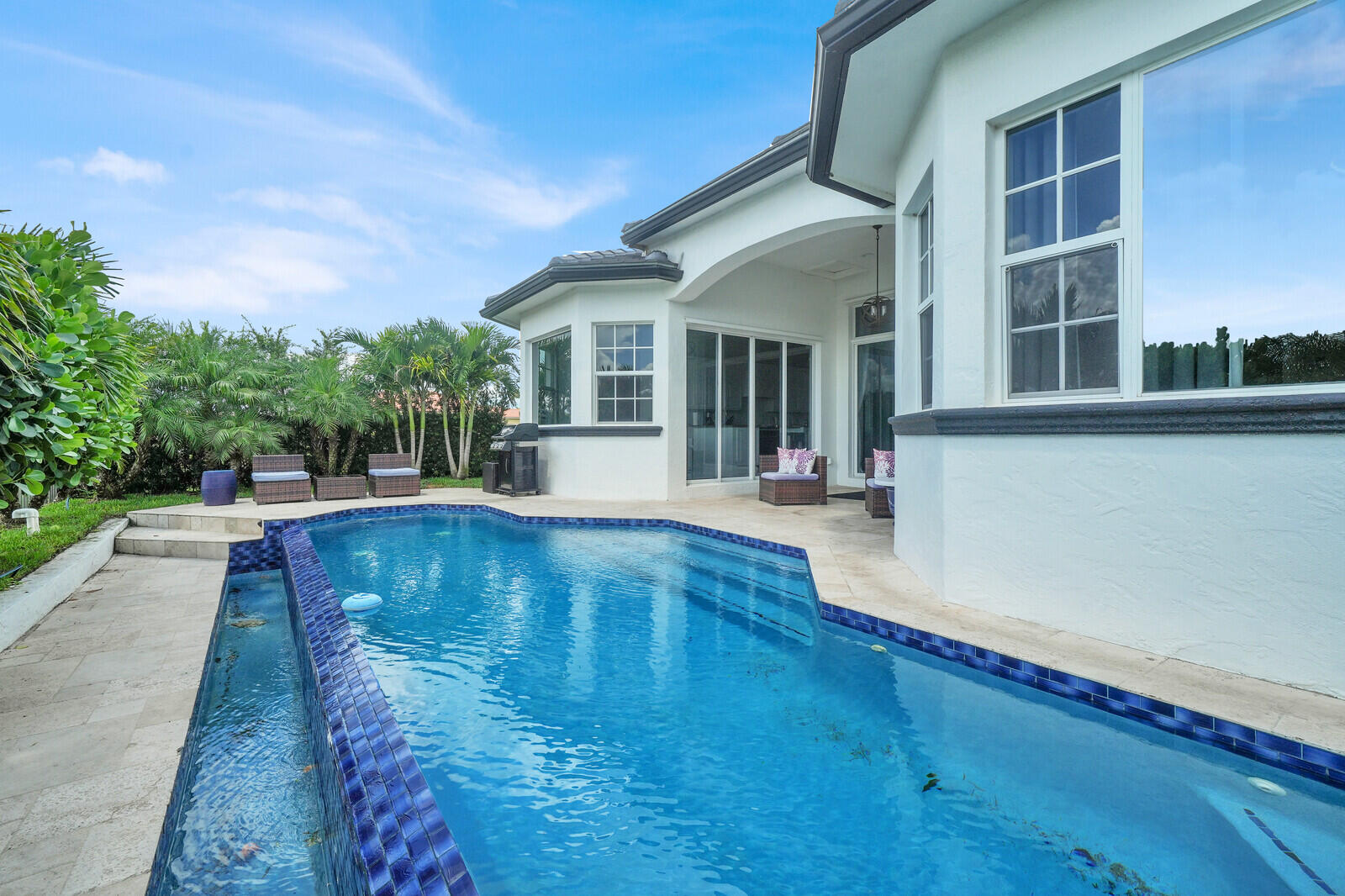 Swimming pool featuring a blue tiled infinity edge and surrounding stone patio