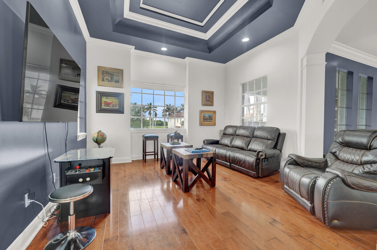 Spacious room featuring wood-finish flooring, white baseboards, and a tray ceiling with recessed lighting