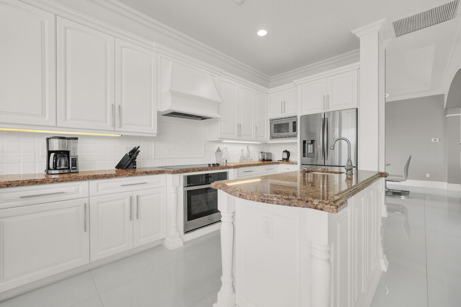 White shaker cabinetry with crown molding, natural stone countertops, stainless steel appliances, a center island, and tile flooring