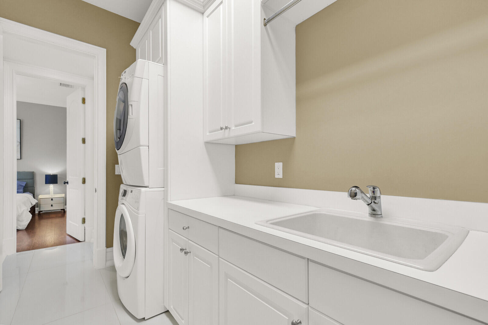 Dedicated laundry space featuring a utility sink with a chrome faucet, white cabinetry, countertop, and stacked appliances