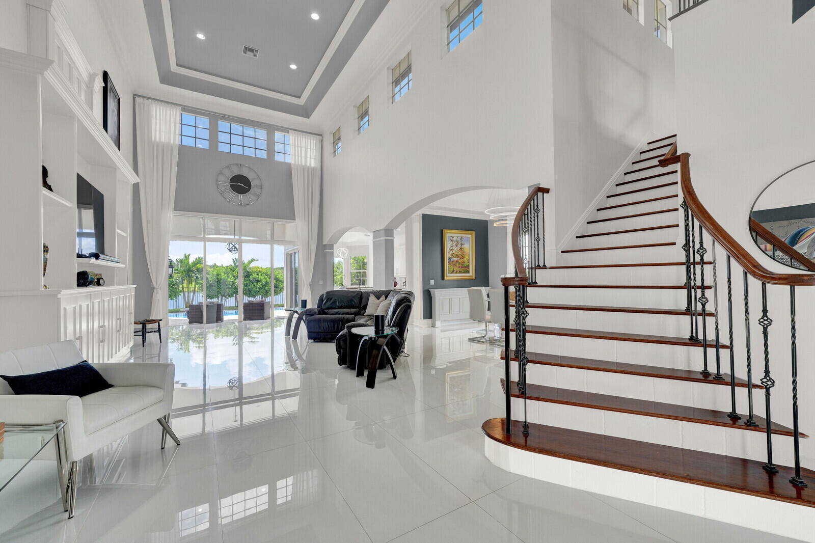 Spacious living area featuring double-height ceilings, large format tile flooring, and a grand staircase with dark wood treads and an ornate iron railing