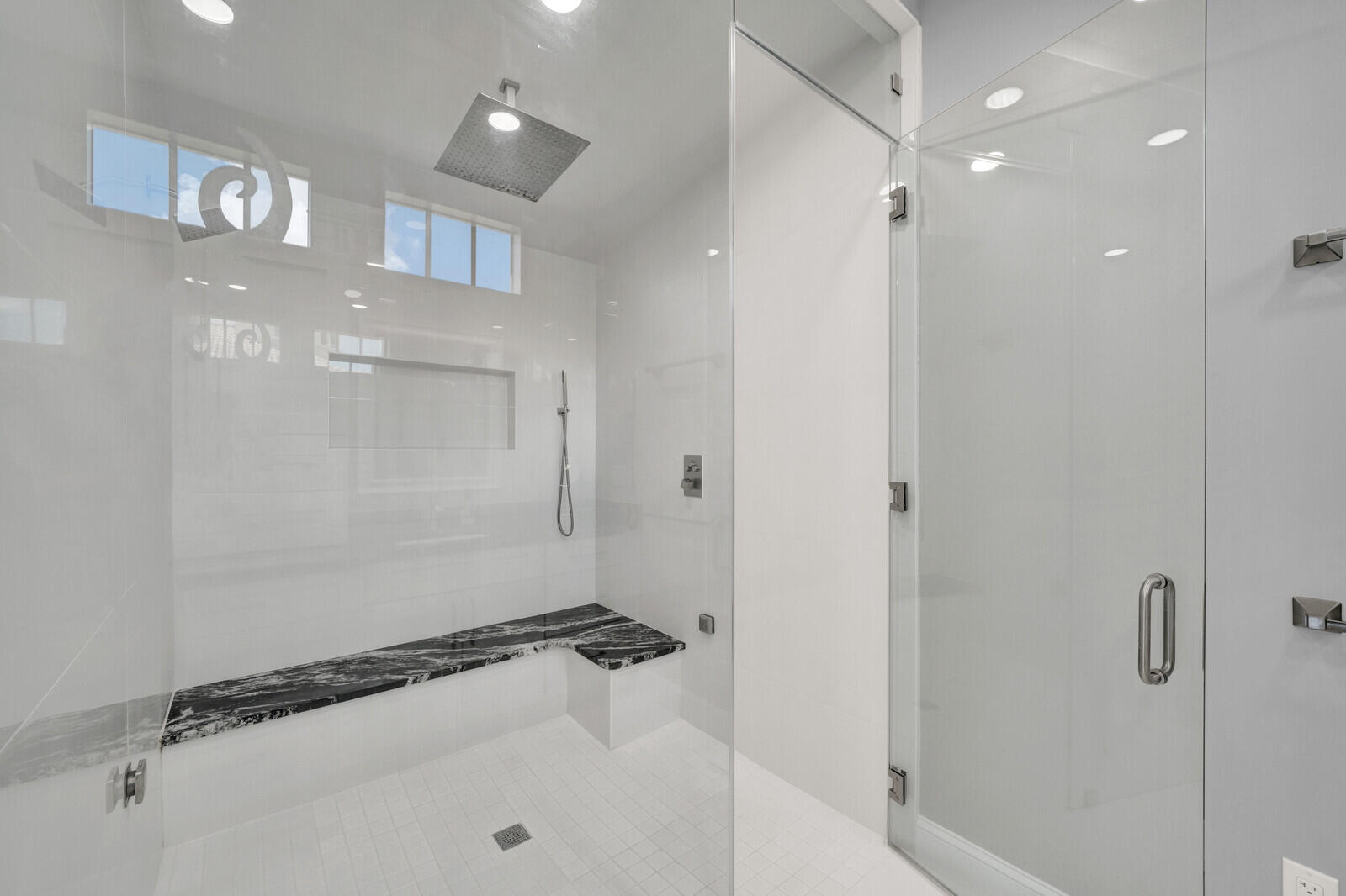 Spacious walk-in shower featuring a rain showerhead, handheld sprayer, and a built-in bench with a dark stone-finish surface